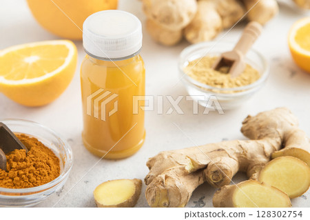 Immune orange and turmeric energy shot drink with ginger root and turmeric powder on light. Immune orange and turmeric energy shot drink with ginger root and turmeric powder on light. 128302754