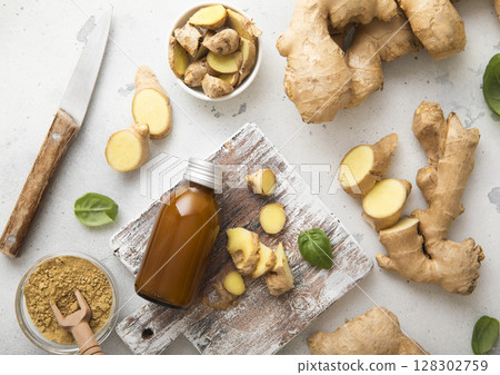 Raw fresh ginger root slices chopped with knife on wooden board with immune energy drink. 128302759