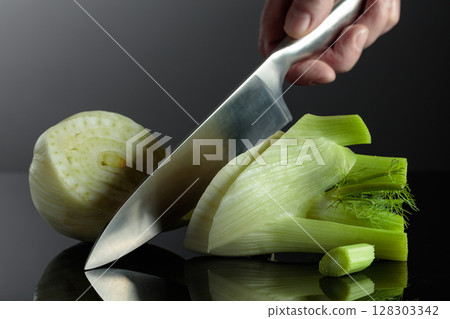 Hand with knife and cut fennel bulb. 128303342