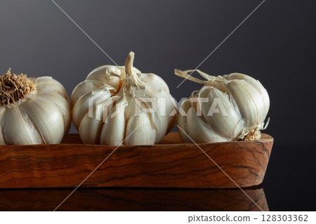 Garlic bulbs in wooden dish on a black background. 128303362