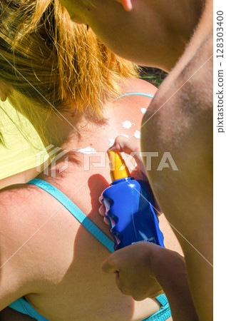 boy Applying sunscreen spray to womans back on a sunny summer day. High quality photo 128303400