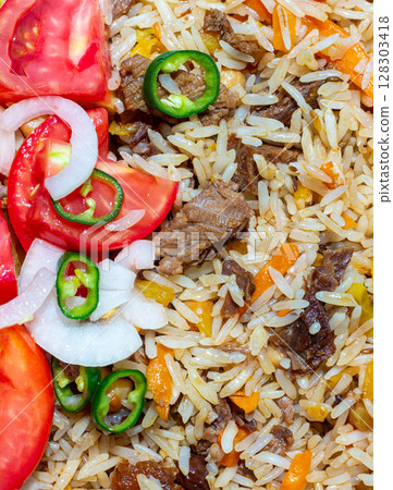 A rice dish with meat, garnished with a salad of chopped tomatoes, onions and hot green chili peppers. The photo is suitable for both the restaurant business and any food related design 128303418