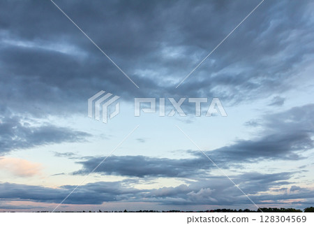 Clouds gathering at sunset over a serene landscape with hints of pink and orange in the sky above the distant horizon 128304569
