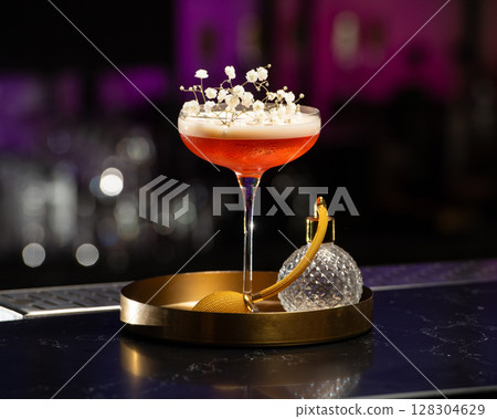 blush-toned cocktail with a frothy top is elegantly garnished with delicate white baby's breath flowers, presented on a golden tray alongside a vintage-style perfume atomizer 128304629