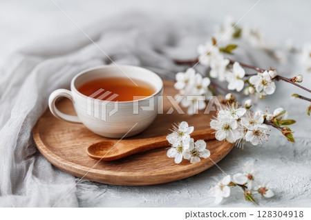 Cup of tea on a wooden plate, with a wooden spoon and white flowers in bloom 128304918