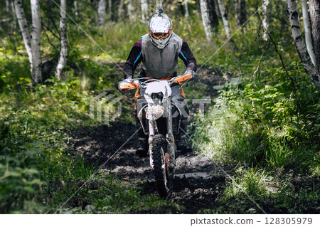Enduro rider on bike speeding through forest trail during an off-road race 128305979