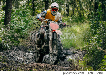 Enduro rider on dirt bike speeding through muddy forest trail during an off-road race Enduro rider on dirt bike speeding through muddy forest trail during an off-road race 128305981