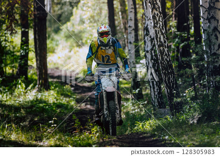 Man enduro rider on dirt bike speeding through forest trail during an off-road race 128305983