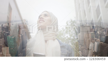 Image of smiling asian woman in hijab using smartphone over cityscape 128306459
