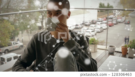 Young man enjoying coffee on balcony, relaxing with city view in background Young man enjoying coffee on balcony, relaxing with city view in background 128306463