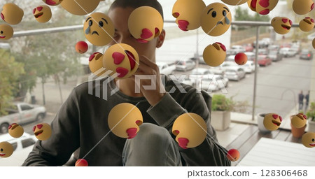 Young man sitting on balcony surrounded by floating emoticons, contemplating life Young man sitting on balcony surrounded by floating emoticons, contemplating life 128306468