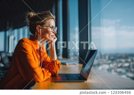 Freelancer in Bright Orange Shirt Thinking While Working on Laptop 128306498