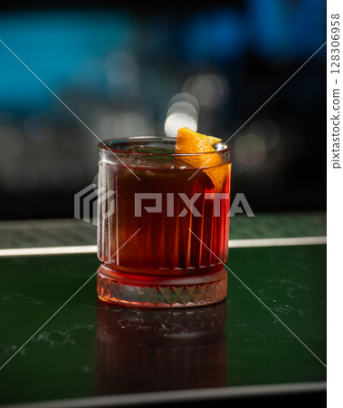 dark red alcoholic cocktail with ice and an orange peel garnish is presented in a rocks glass 128306958