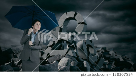 Holding umbrella, businesswoman stands near large broken pound sign under stormy sky 128307554