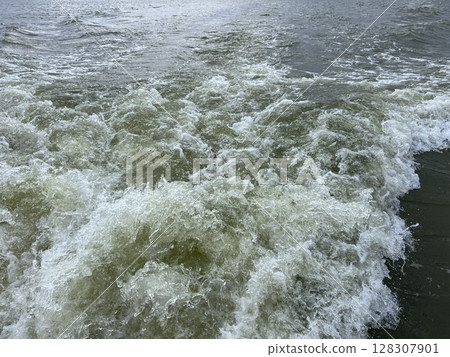 Close up photo of White Turbulent ocean waves crash and churn, creating a powerful display of frothy white water against the dark, deep sea taken from after a ferry on ocean under cloudy day oversea Close up photo of White Turbulent ocean waves crash and churn, creating a powerful display of frothy white water against the dark, deep sea taken from after a ferry on ocean under cloudy day oversea 128307901