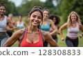 A group of people running in a green park, with a smiling woman in the foreground wearing a red sports bra. - Generic AI Image 128308833