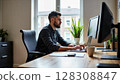 A focused man with a beard works diligently on his laptop at a wooden desk in a bright home office setup. - Generic AI Image 128308847