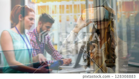Using virtual reality headset, woman interacting with digital interface over office workers 128308883