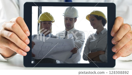 Hands holding digital tablet showing architect discussing plans over blueprint Hands holding digital tablet showing architect discussing plans over blueprint 128308892