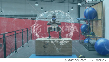 Human brain spinning against african american man wearing face mask jumping on plyo box at gym 128309347