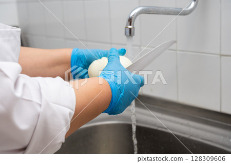 women's hands clean onions with a knife under the tap with water in the sink at a commercial kitchen 128309606