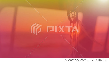 Image of dream catcher moving in wind with yellow to red hue with sunset in background Image of dream catcher moving in wind with yellow to red hue with sunset in background 128310732