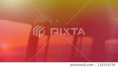 Image of mirror ball moving in wind with yellow to red hue with sunset in background 128310734