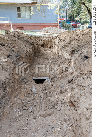 A trench dug in front of the facade of an apartment building. Excavation work. Repair work on a heating main. A trench dug in front of the facade of an apartment building. Excavation work. Repair work on a heating main. 128311257
