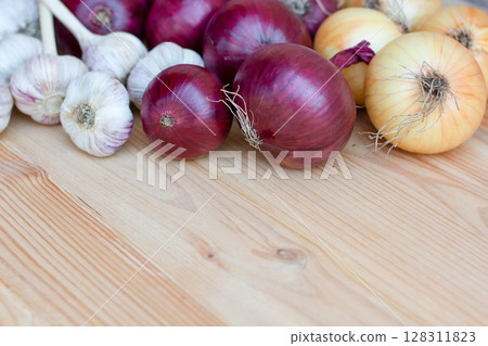Red and yellow onions with garlic lie on a wooden background harvest. Copy space 128311823