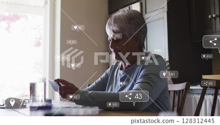 Image of social media icons and numbers on banners over senior woman using smartphone Image of social media icons and numbers on banners over senior woman using smartphone 128312445
