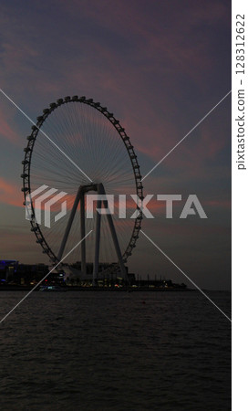 A stunning sunset silhouette of a Ferris Wheel positioned beautifully by the waters edge 128312622