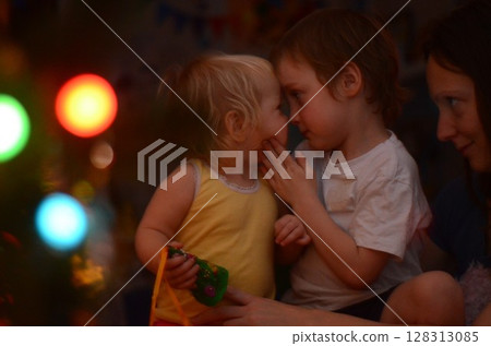 Children Sharing a Sweet Moment by Christmas Tree Children Sharing a Sweet Moment by Christmas Tree 128313085