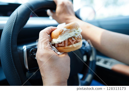 Asian woman driver hold and eat hamburger in car, dangerous and risk an accident. Asian woman driver hold and eat hamburger in car, dangerous and risk an accident. 128313173
