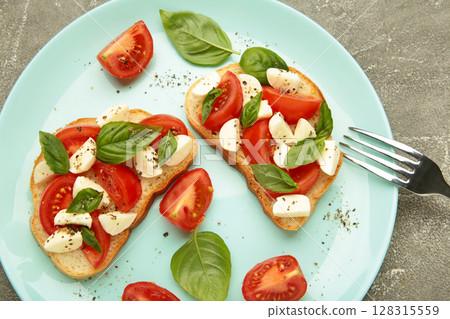 Tasty sandwich with mozzarella cheese, tomatoes and basil on mint plate on grey background. Caprese 128315559