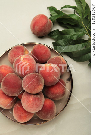 Sweet peaches and leaves on dark plate on light background. Space for text Sweet peaches and leaves on dark plate on light background. Space for text 128315567