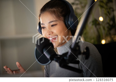 Podcasting. Joyful woman recording her podcast with a microphone and headphones. 128316075