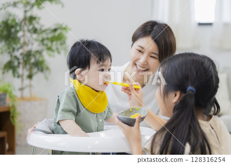 Mother and siblings feeding baby food 128316254