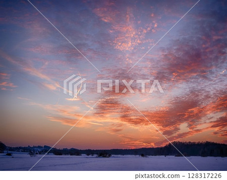 A beautiful sunset over a snowy landscape with a few trees in the background 128317226