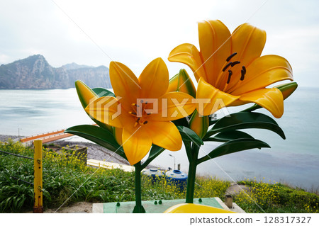 Vibrant Yellow Daylily Sculptures with Coastal Mountain Scenery 128317327