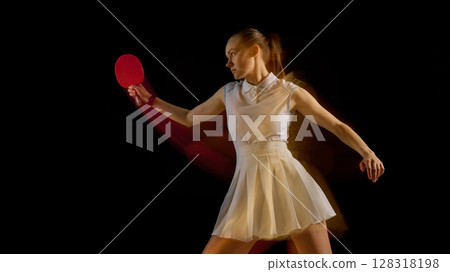 Table tennis player swinging paddle with motion blur in athletic pose on dark background 128318198