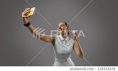 Smiling female table tennis player taking selfie with ball in hand on gray background 128318229