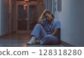 Exhausted nurse reflects on burnout and emotional strain while sitting on the hospital floor after a long shift 128318280