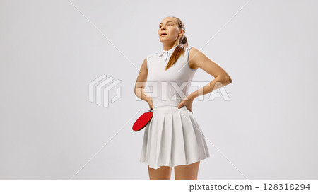 Tired female table tennis player resting with paddle in white dress on neutral background 128318294