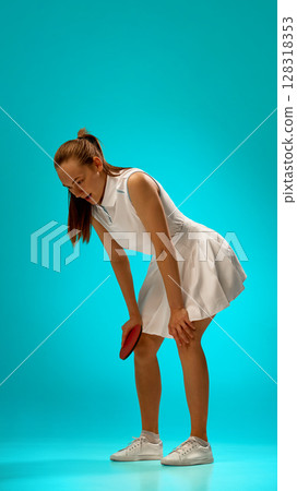 Tired female tennis player in white dress on turquoise background 128318353