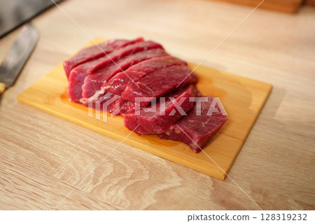 A piece of fresh beef is placed on a wooden cutting board in a bright kitchen. 128319232