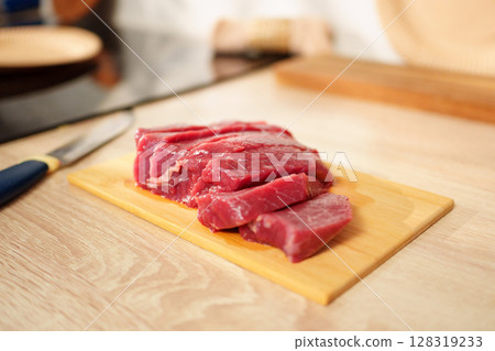 Freshly sliced raw beef laid on a wooden cutting board ready for cooking or preparation in a kitchen setting 128319233