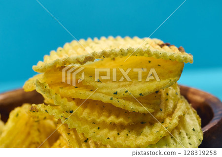 Crunchy potato chips stacked neatly with a golden hue and flecks of seasoning visible in close-up detail 128319258