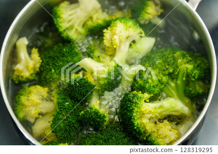 Cooking fresh broccoli in a saucepan over medium heat during a sunny afternoon 128319295