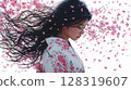 一位身著和服的年輕女子站在飄落的櫻花花瓣中 128319607