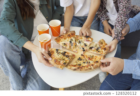 Top view of family members reaching for hot pizza slices, enjoying delicious food together at home. Top view of family members reaching for hot pizza slices, enjoying delicious food together at home. 128320112